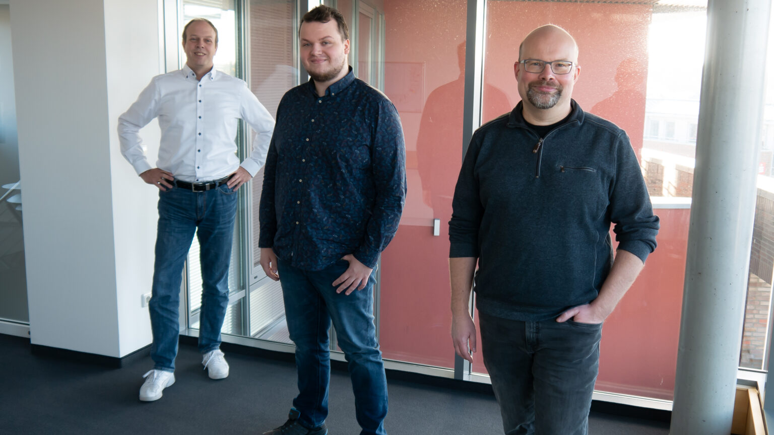Drei Mitarbeiter von Amagno stehen in einem modernen Büro und repräsentieren das Team für Dokumentenmanagement und digitale Archivierung.